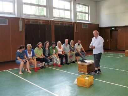 Dr. Klaus Mönkemeyer zeigt den auf einer Sportbank sitzenden Teilnehmern eine Übung