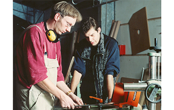Zwei Männer arbeiten an einer Werkbank (vergrößerte Bildansicht wird geöffnet)
